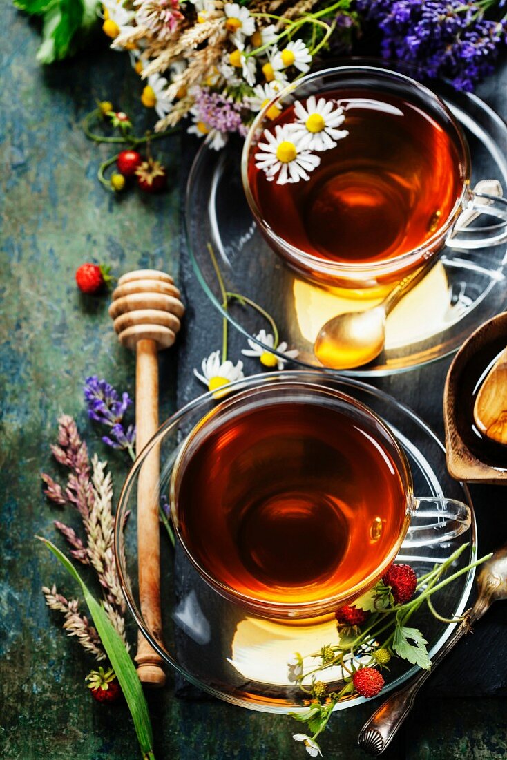 Kräutertee mit Honig, umgeben von Waldbeeren und Wiesenblumen