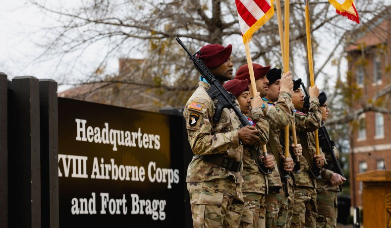 U.S. Army XVIII Airborne Corps color guard stands at attention holding rifles and flags in front of the Headquarters Fort Bragg sign during a redesignation ceremony.
